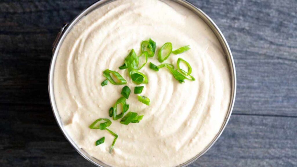 An overhead view of a bowl filled with white bean hummus, garnished with sliced, green onions.