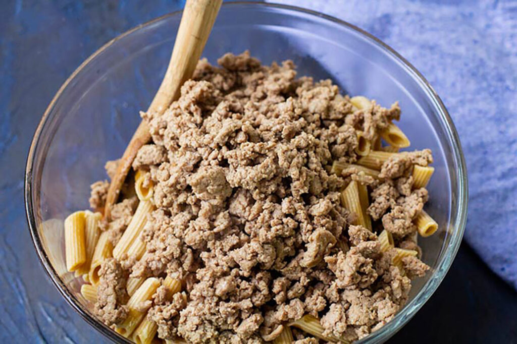 Cooked ground turkey added to cooked pasta in a mixing bowl.