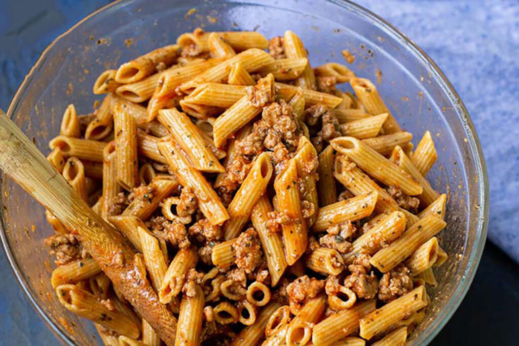 Ground turkey and cooked pasta mixed with sauce in a mixing bowl.