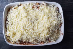 A white casserole dish filled with zit blend and topped with shredded mozzarella.
