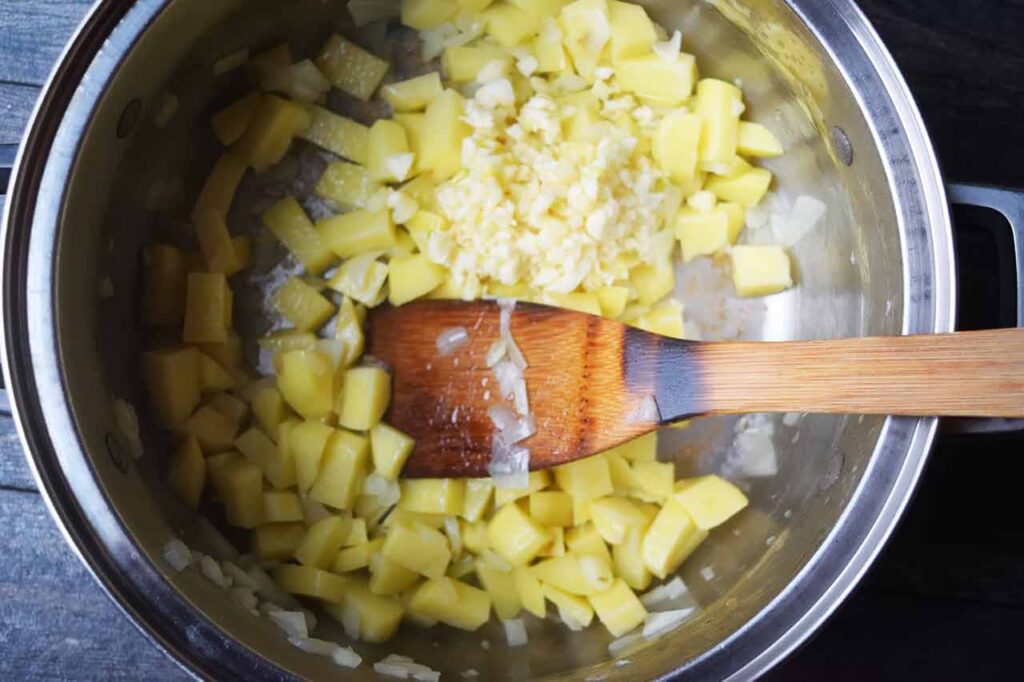 Minced garlic added to potatoes and onions in a large pot.