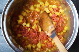 Spices and diced tomatoes added to a large pot of potatoes, garlic and onions.