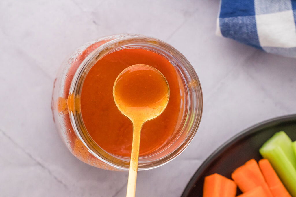 An overhead view of a spoon lifting some buffalo sauce out of a jar.