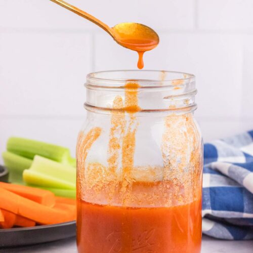 A spoon drips some buffalo sauce into a jar full of it.