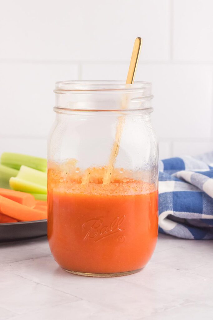 A long spoon sits in a jar of buffalo sauce.