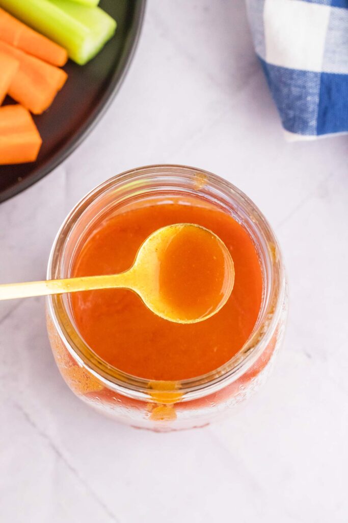 An overhead view of a spoon lifting some buffalo sauce out of a jar.