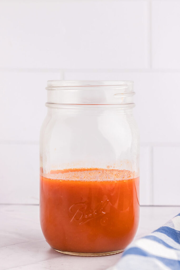 A side view of an open canning jar half filled with buffalo sauce.