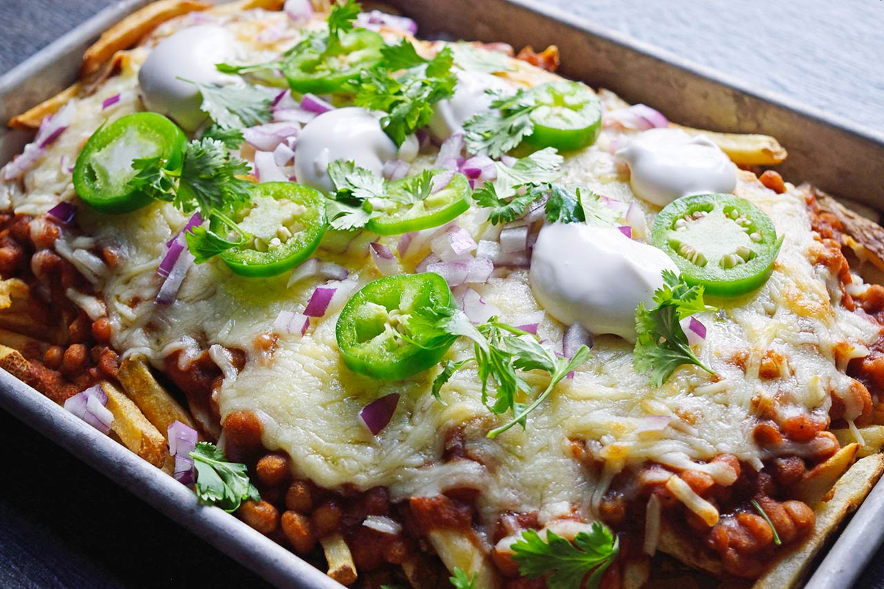 Chili Cheese Fries just out of the oven and garnished with dollops of sour cream, slices of jalapeno pepper, diced red onion, and fresh cilantro.