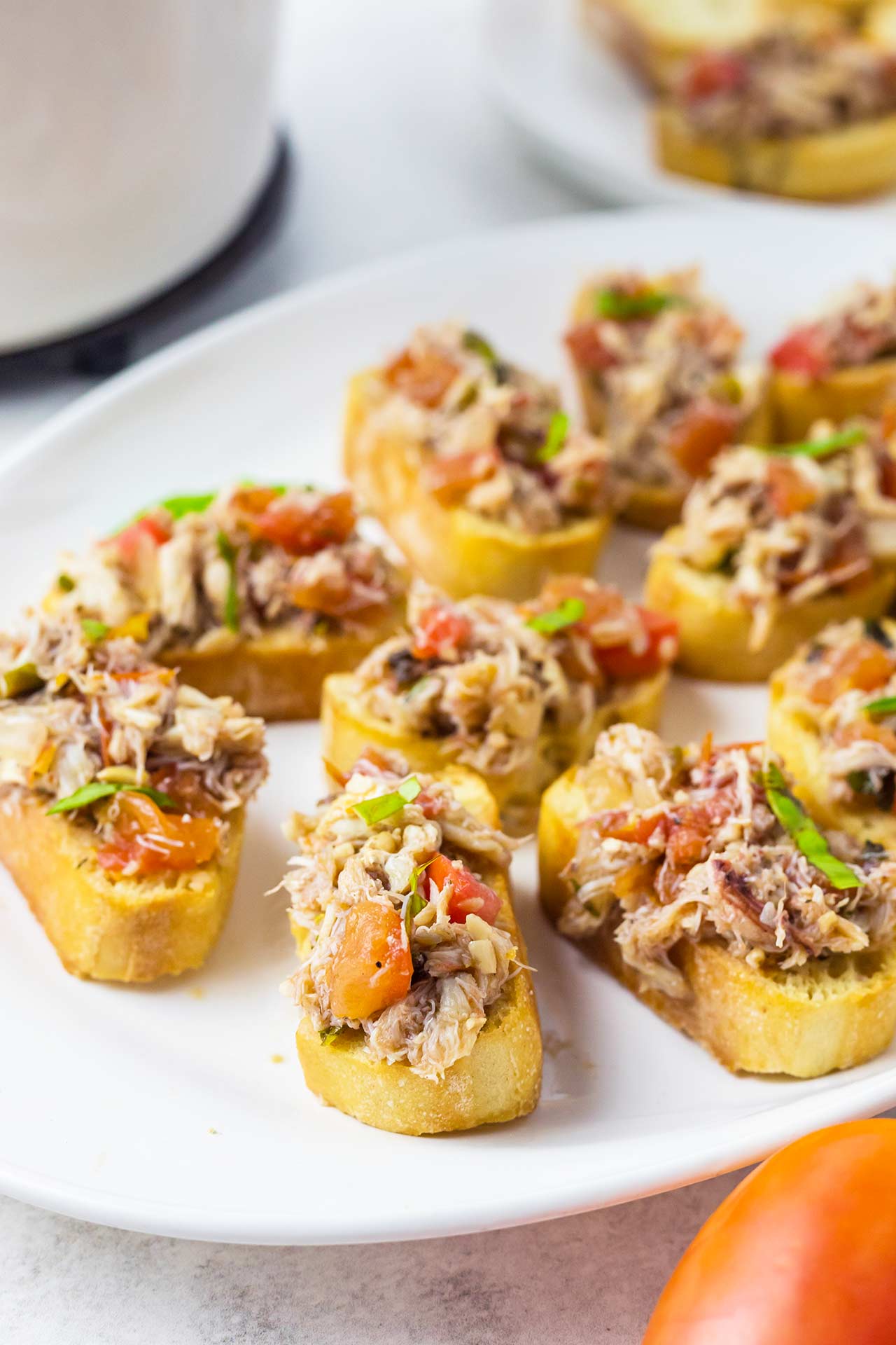 A white platter filled with multiple crab crostini.