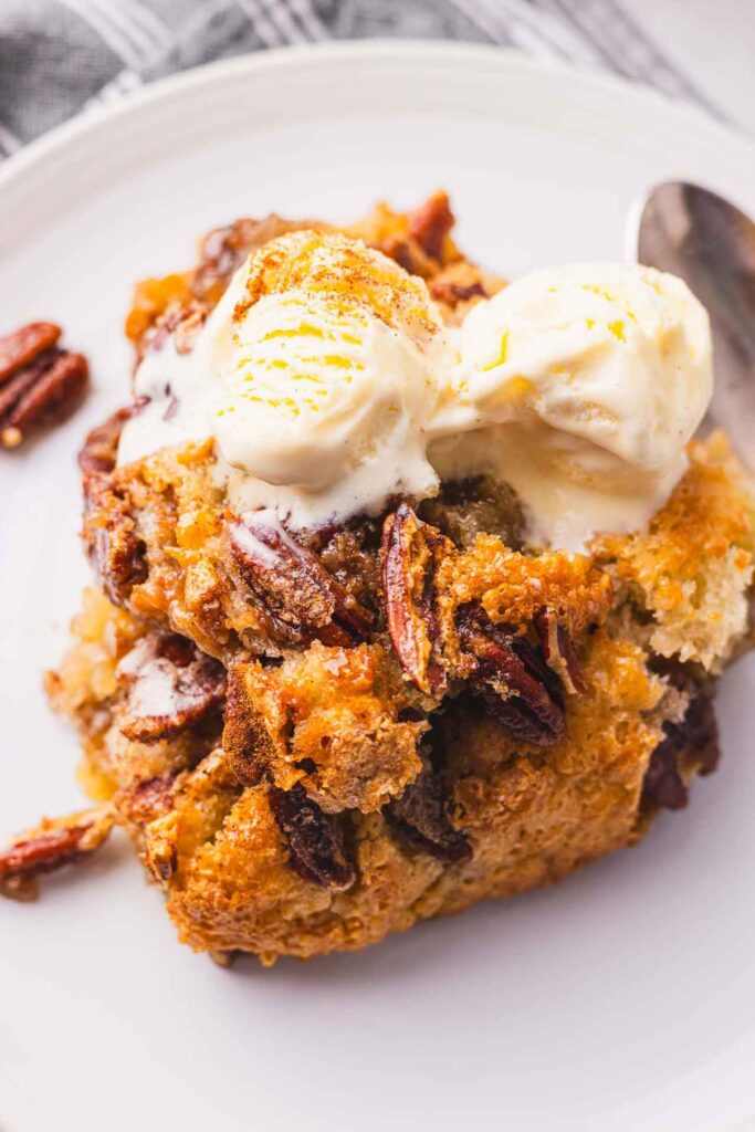 A plate with a slice of pecan cobbler with ice cream on it.