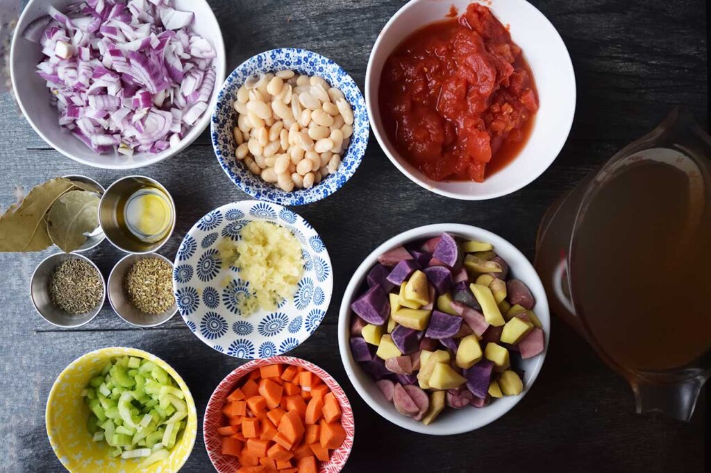 Chunky Fish Stew Recipe ingredients in individual bowls on a gray surface.