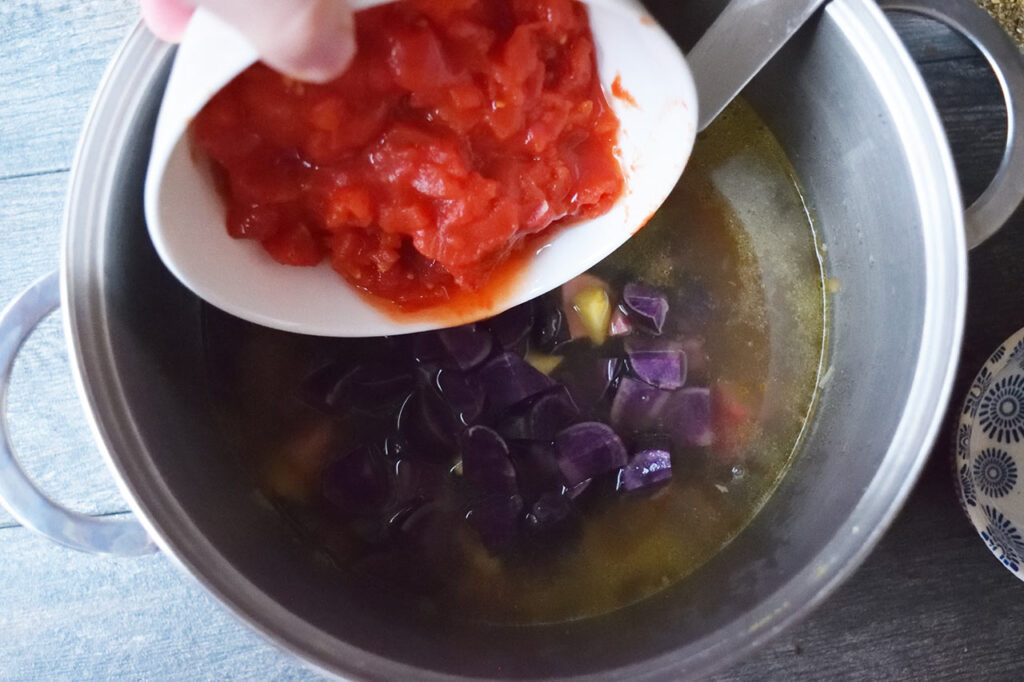 Adding diced tomatoes to the soup pot.