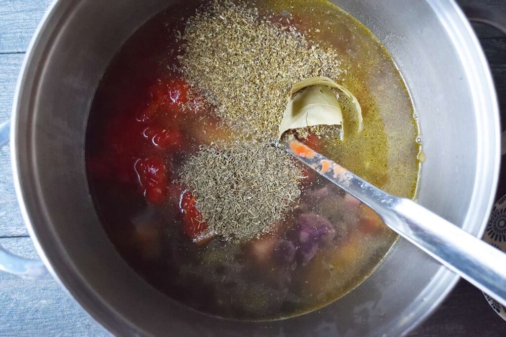 Spices added to stock and vegetables in a soup pot.