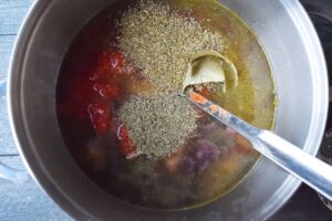 Spices added to stock and vegetables in a soup pot.