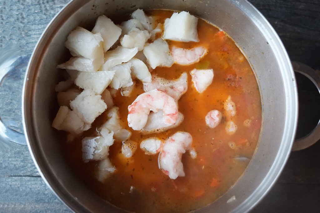 Cod and shrimp added to stock and veggies in a soup pot.