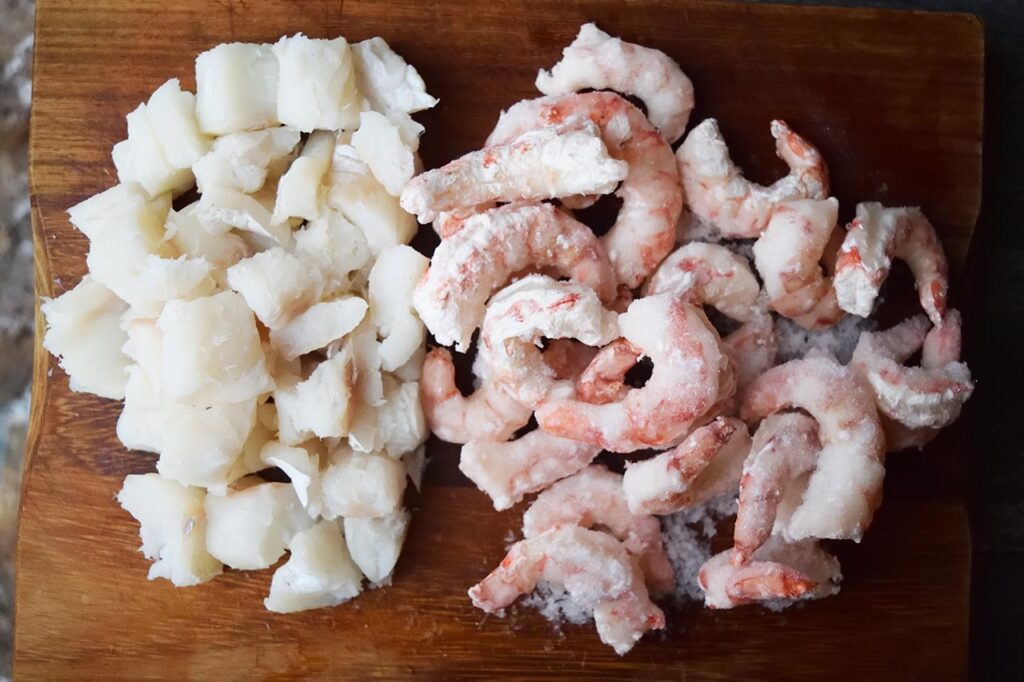 Fresh cod chunks and frozen shrimp on a cutting board.