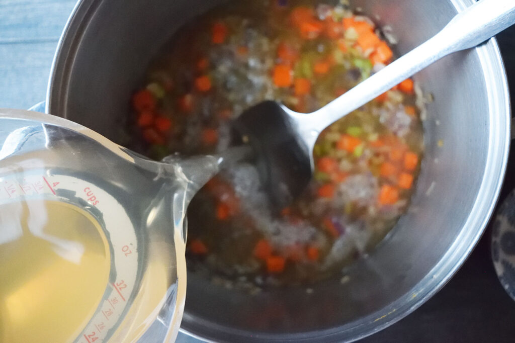 Pouring fish stock into a soup pot with saut&eacute;d vegetables.