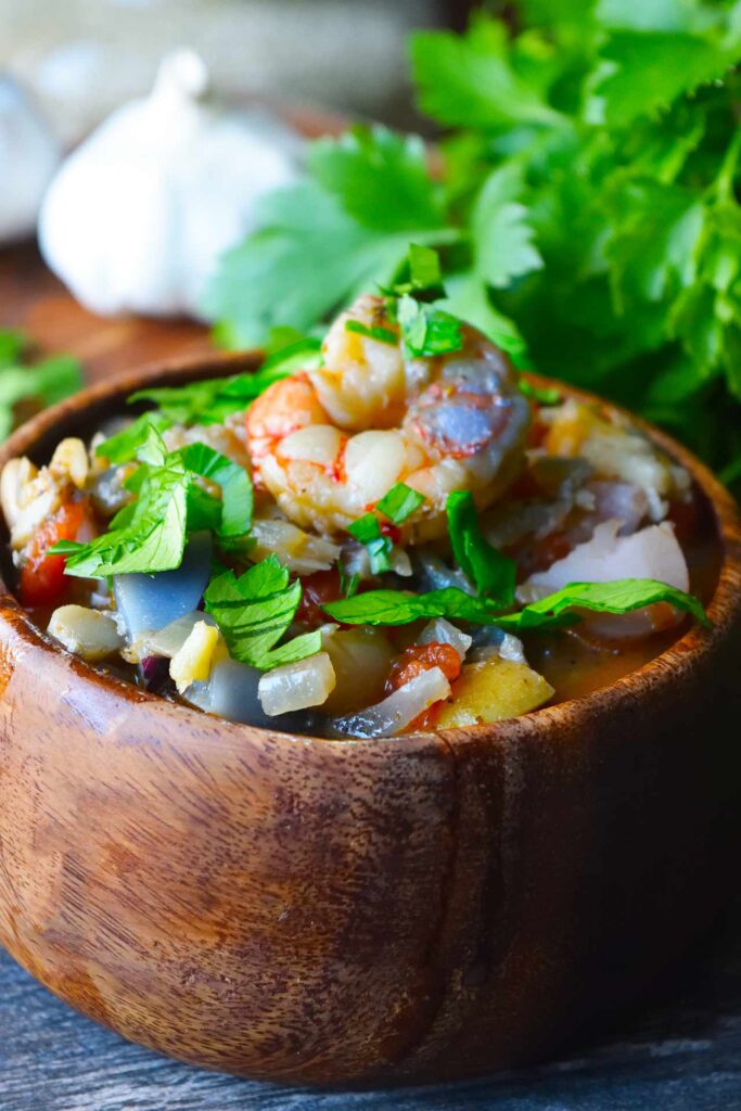 A front view of a wood bowl filled with Chunky Fish Stew and garnished with fresh parsley.