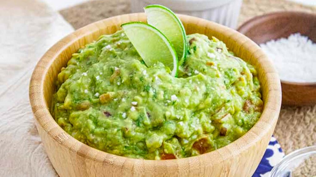 A wood bowl filled with guacamole and garnished with two lime wedges.