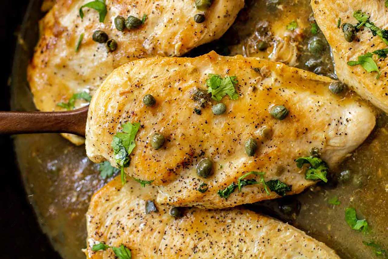 Lemon caper chicken breasts in a cast iron skillet.