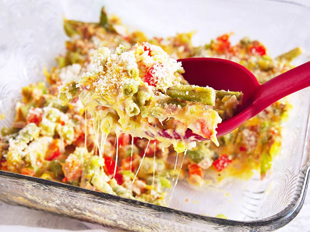 A red serving spoon holds a scoop of No Noodle Tuna Casserole over a full casserole dish.