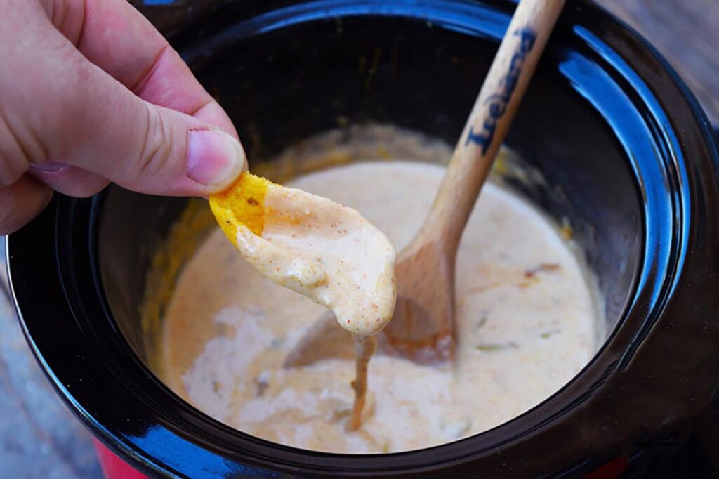 A hand dips a corn chip into homemade queso.