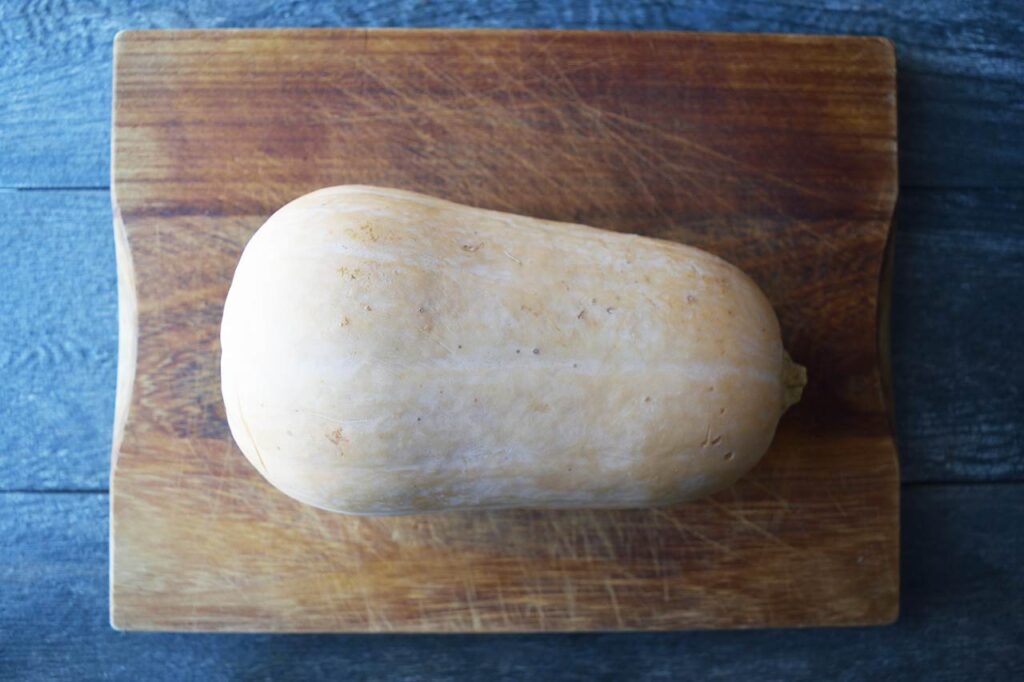 A full butternut squash laying on a cutting board.