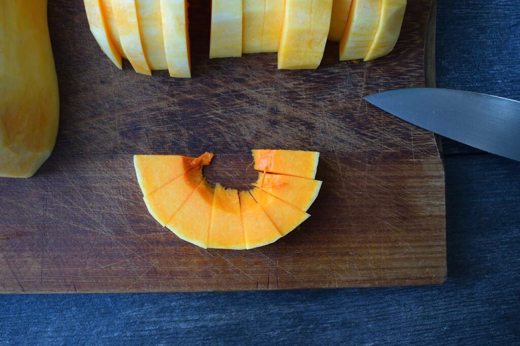 A half circle slice of butternut squash sliced on a cutting board.