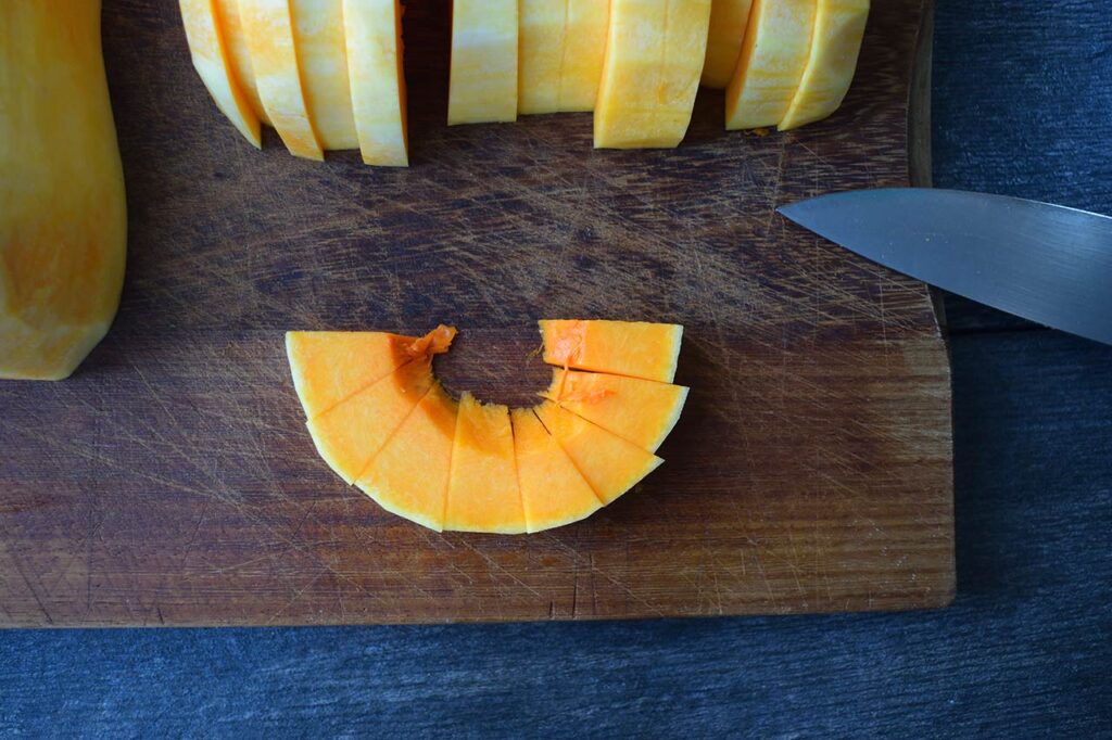 A half circle slice of butternut squash sliced on a cutting board.