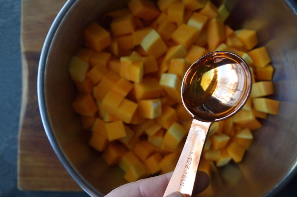 Adding oil to butternut squash cubes in a mixing bowl.