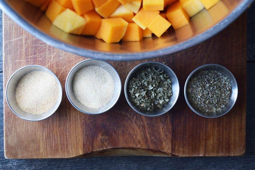 Herbs for this Roasted Butternut Squash recipe in individual bowls sitting next to a bowl of butternut squash cubes.