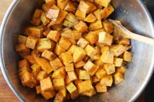 Butternut squash cubes mixed with oil and spices in a mixing bowl.