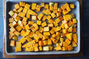 Spiced and oiled butternut squash cube in a single layer on a sheet pan.