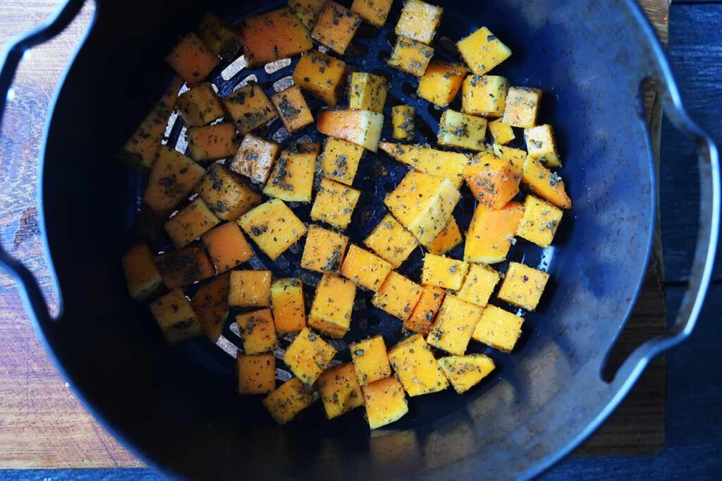 Cubes of butternut squash sitting in a single layer in an air fryer basket.