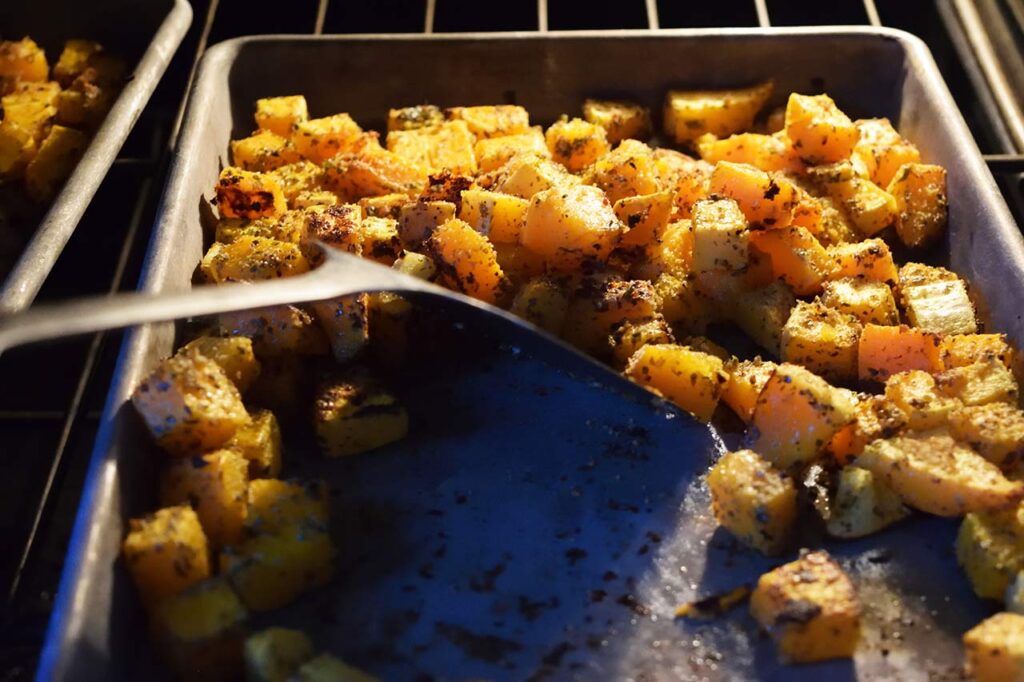 Stirring Roasted Butternut Squash on a sheet pan in an oven.