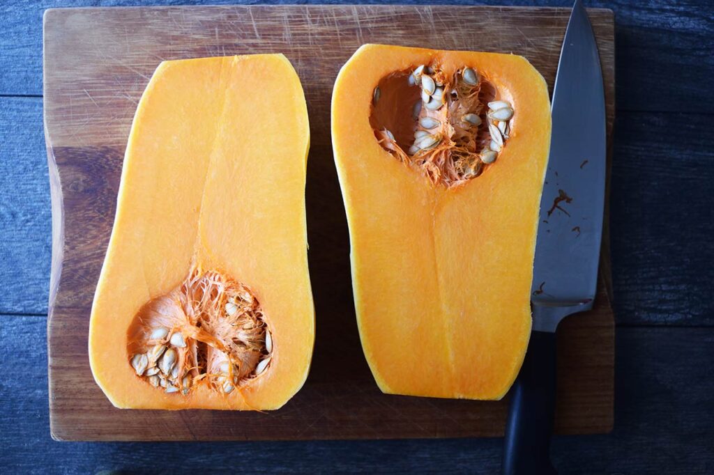 A butternut squash cut in half laying on a cutting board.