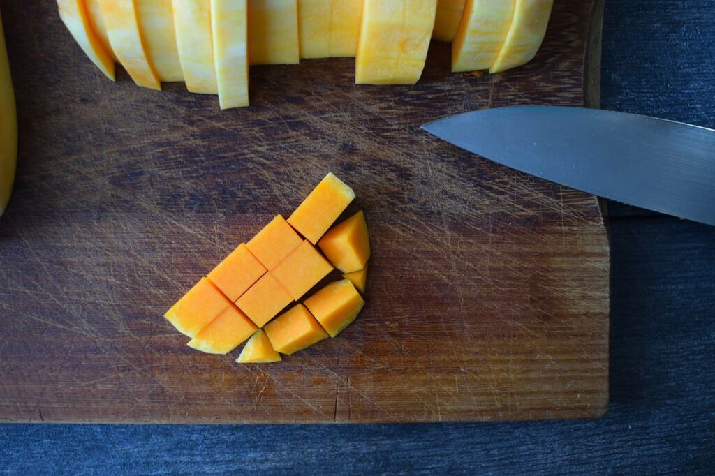 A slice of butternut squash cut into cubes and laying on a cutting board.