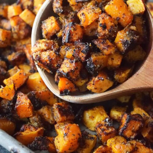 A scoop of Roasted Butternut Squash lays on a sheet pan full of squash.