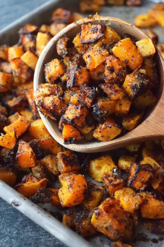 A scoop of Roasted Butternut Squash lays on a sheet pan full of squash.