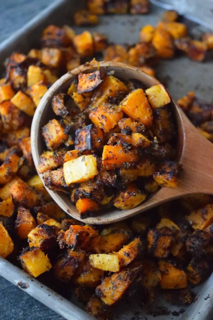 Roasted Butternut Squash fills a wooden spoon laying on a sheet pan full of roasted squash.