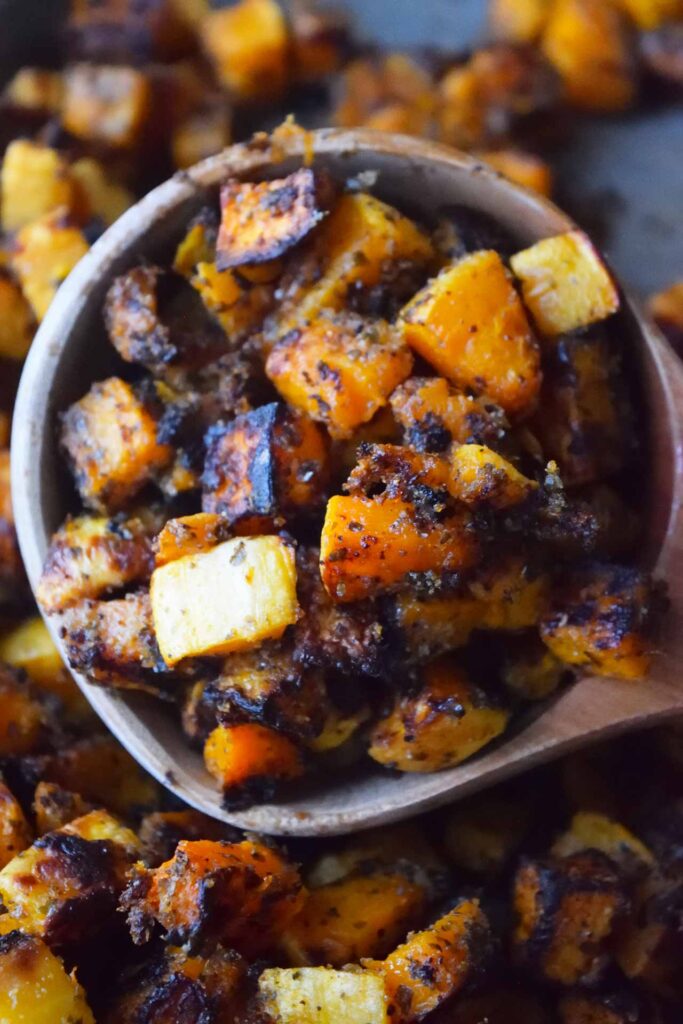 A closeup of a wooden scoop filled with Roasted Butternut Squash.