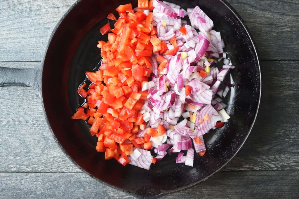 Diced onion and red bell pepper in a cast iron skillet.