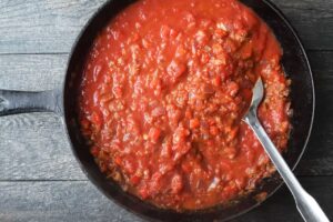 A cast iron skillet full of Shakshuka sauce. A serving spoon rests in the sauce.