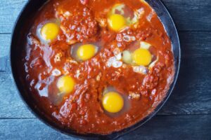 Raw eggs nestled into wells made in the Shakshuka sauce.