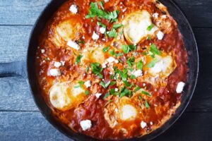 The finished Shakshuka garnished with fresh, chopped parsley and feta cheese crumbles.