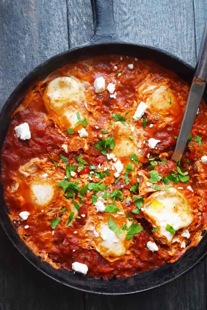 An overhead view of a cast iron skillet full of Shakshuka. A serving spoon rests in the skillet.