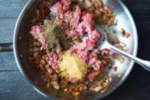 Spices added to ground meat and onions in a skillet.