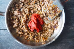 Tomato paste added to browned meat and onions in a skillet.