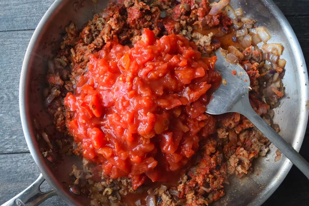 Diced tomatoes added to a skillet with meat and onions in it.