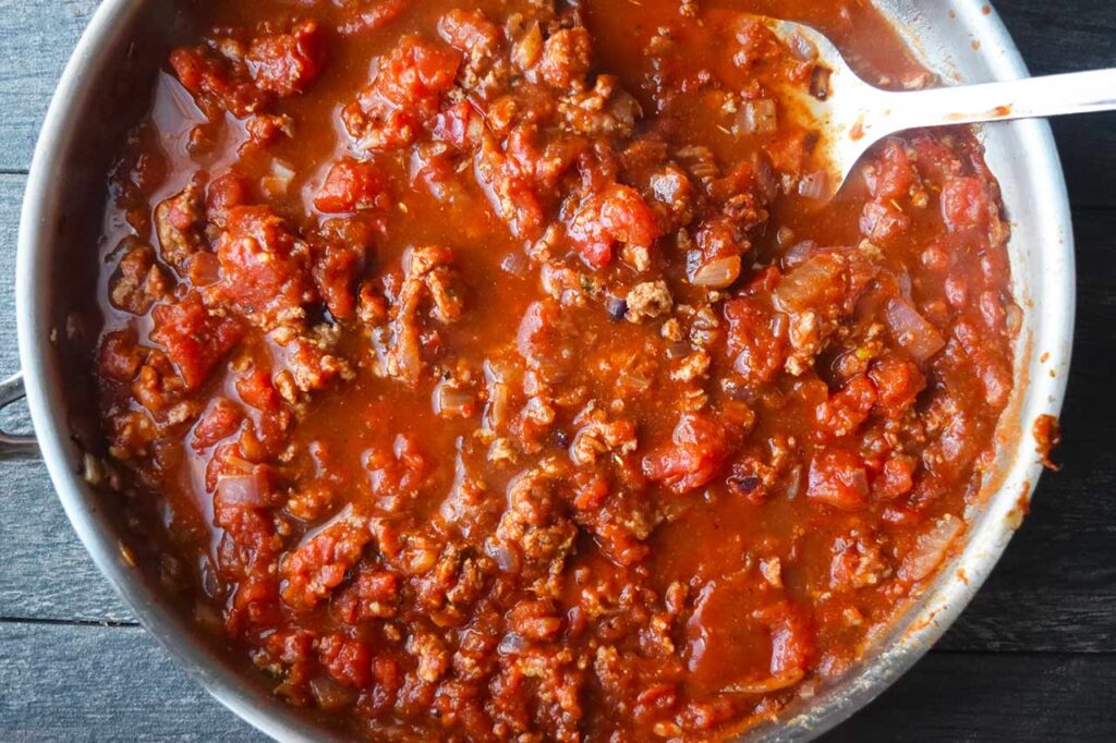 Broth added to spaghetti sauce in a skillet.